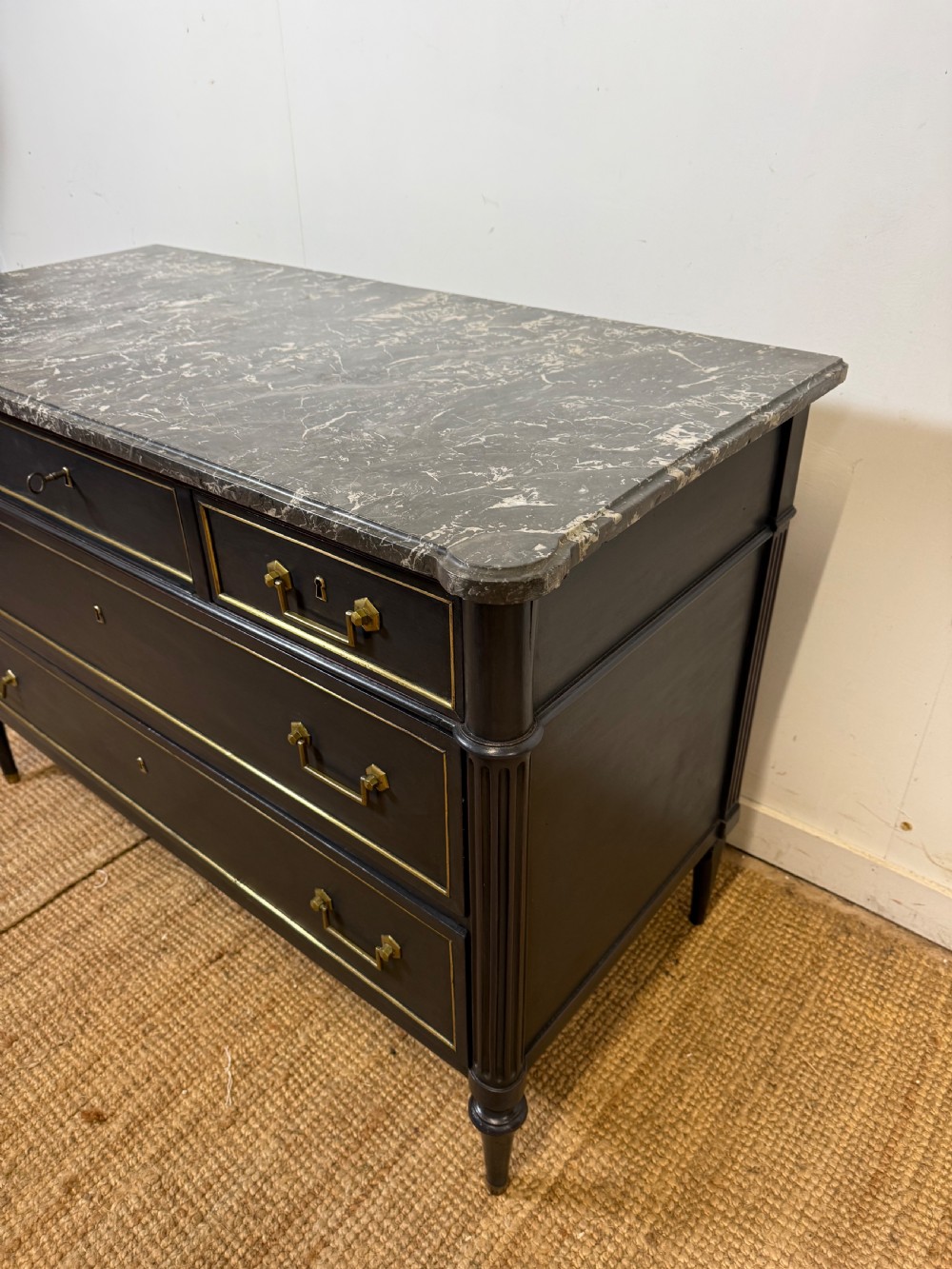 An early 19th-century black painted Louis XVI style commode featuring a grey marble top, brass trim, and fluted column legs. View II