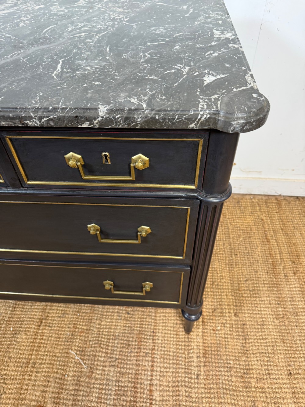 An early 19th-century black painted Louis XVI style commode featuring a grey marble top, brass trim, and fluted column legs. View III
