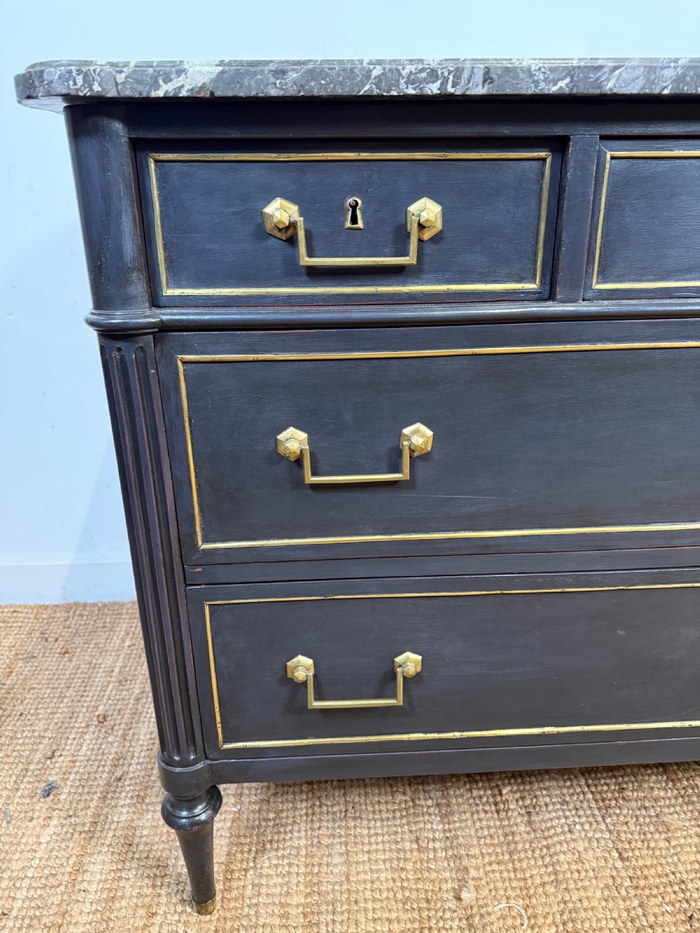 An early 19th-century black painted Louis XVI style commode featuring a grey marble top, brass trim, and fluted column legs. View V