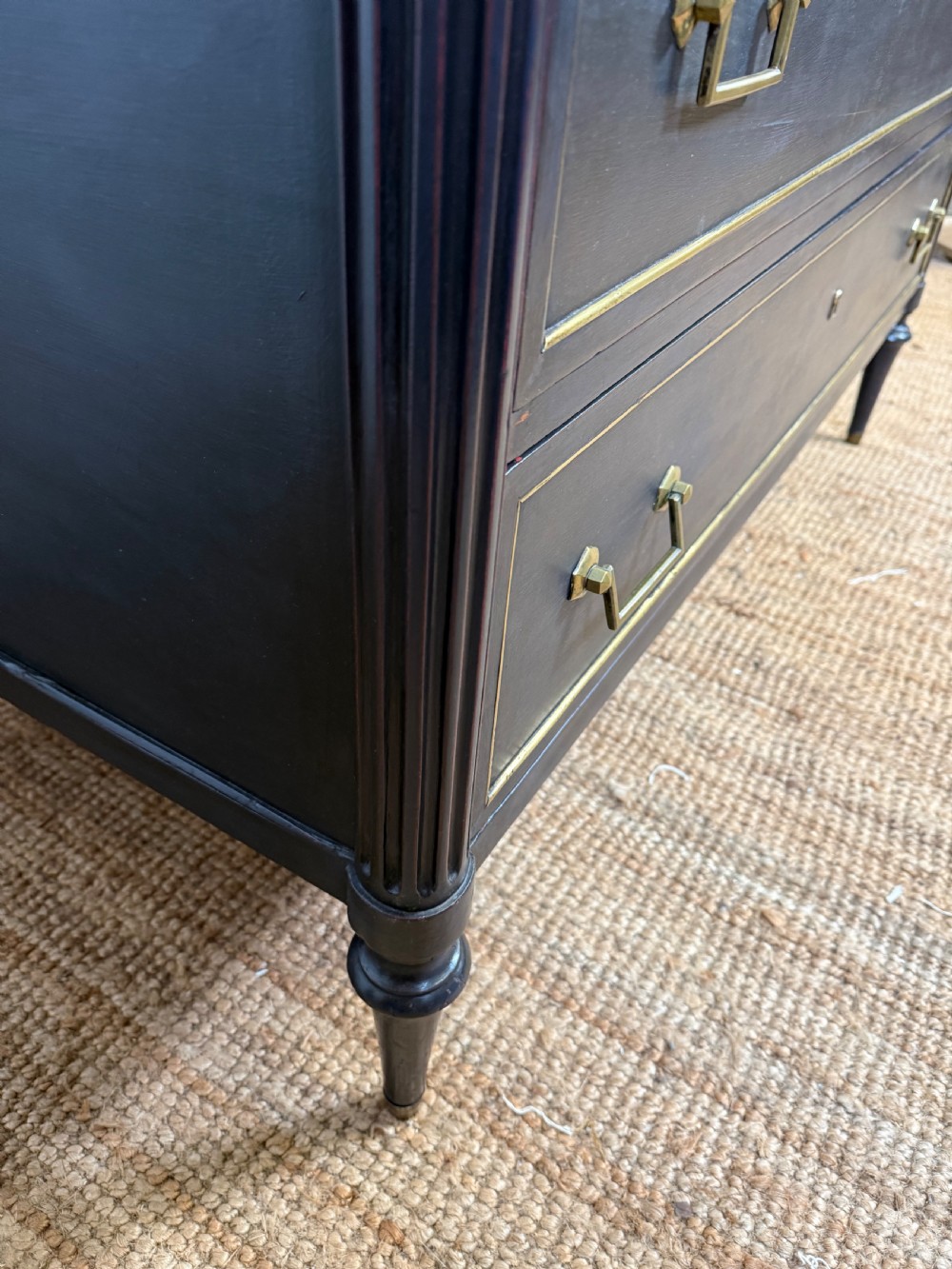 An early 19th-century black painted Louis XVI style commode featuring a grey marble top, brass trim, and fluted column legs. View VI
