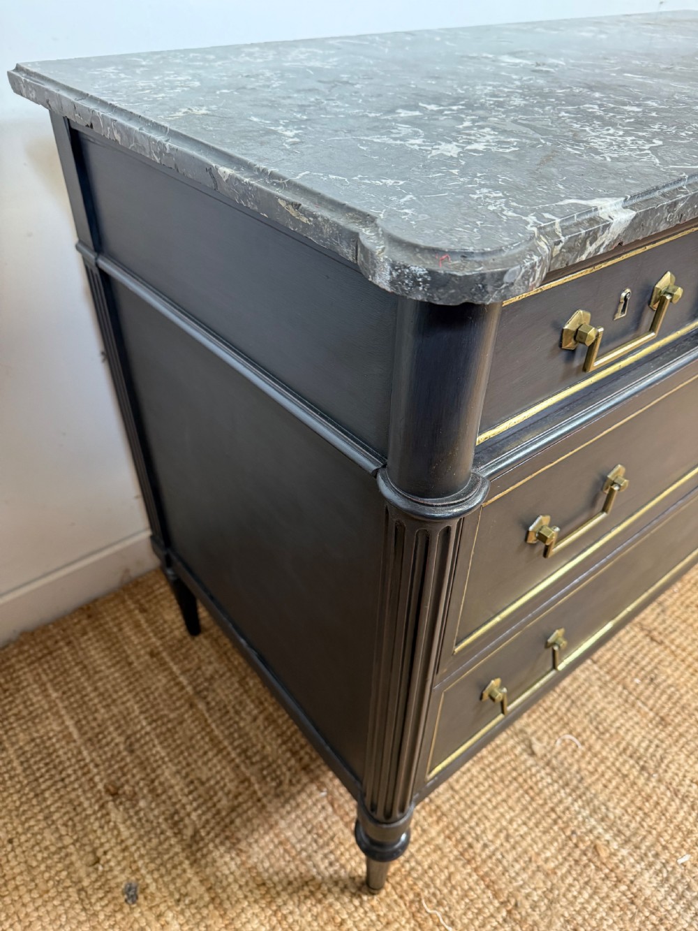 An early 19th-century black painted Louis XVI style commode featuring a grey marble top, brass trim, and fluted column legs. View VIII