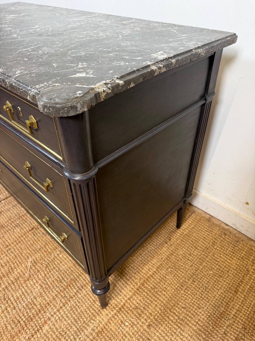 An early 19th-century black painted Louis XVI style commode featuring a grey marble top, brass trim, and fluted column legs. View IX