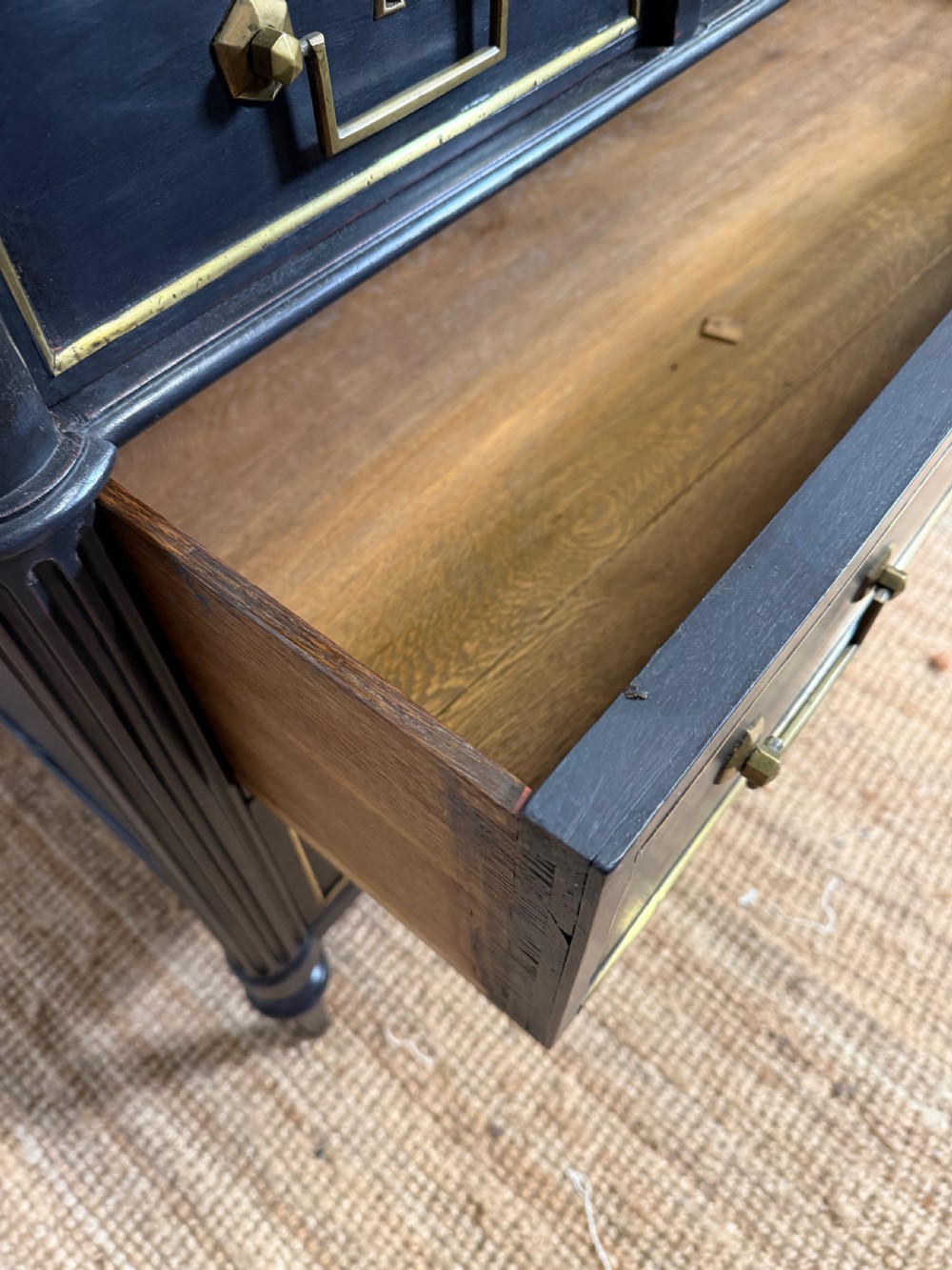 An early 19th-century black painted Louis XVI style commode featuring a grey marble top, brass trim, and fluted column legs. View X