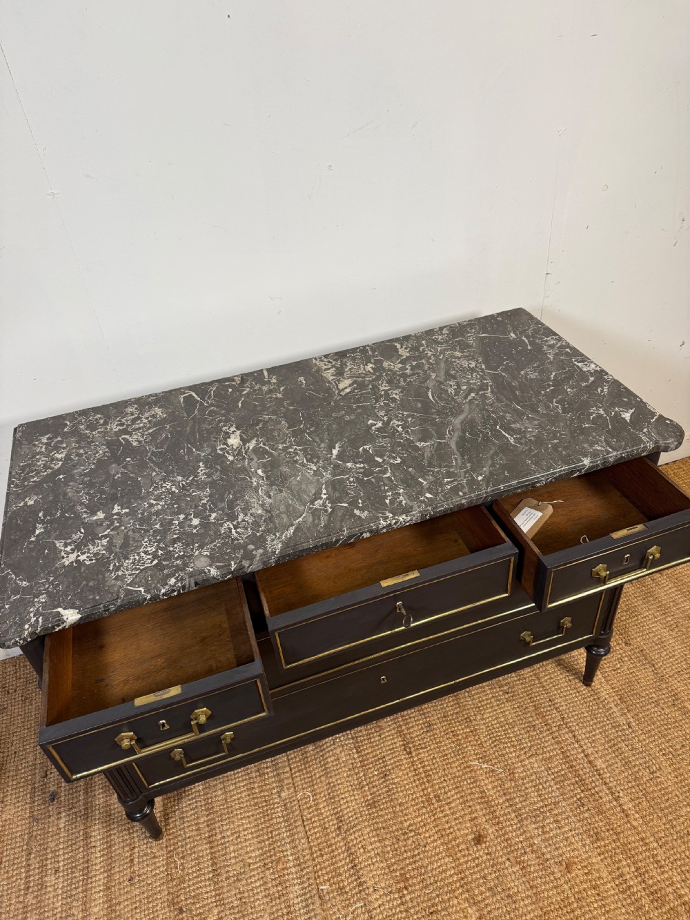 An early 19th-century black painted Louis XVI style commode featuring a grey marble top, brass trim, and fluted column legs. View XI