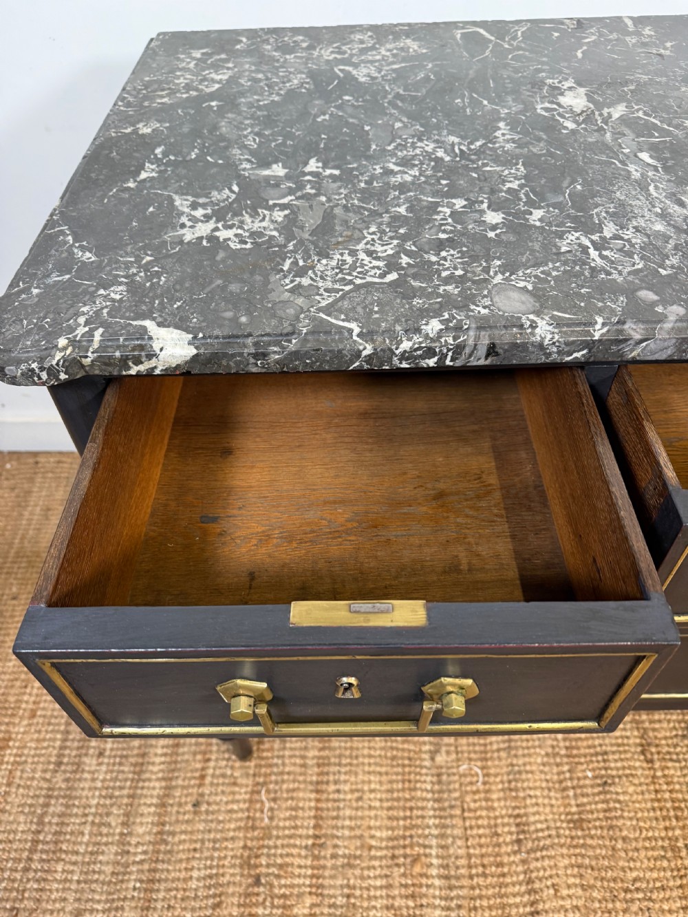 An early 19th-century black painted Louis XVI style commode featuring a grey marble top, brass trim, and fluted column legs. View XII