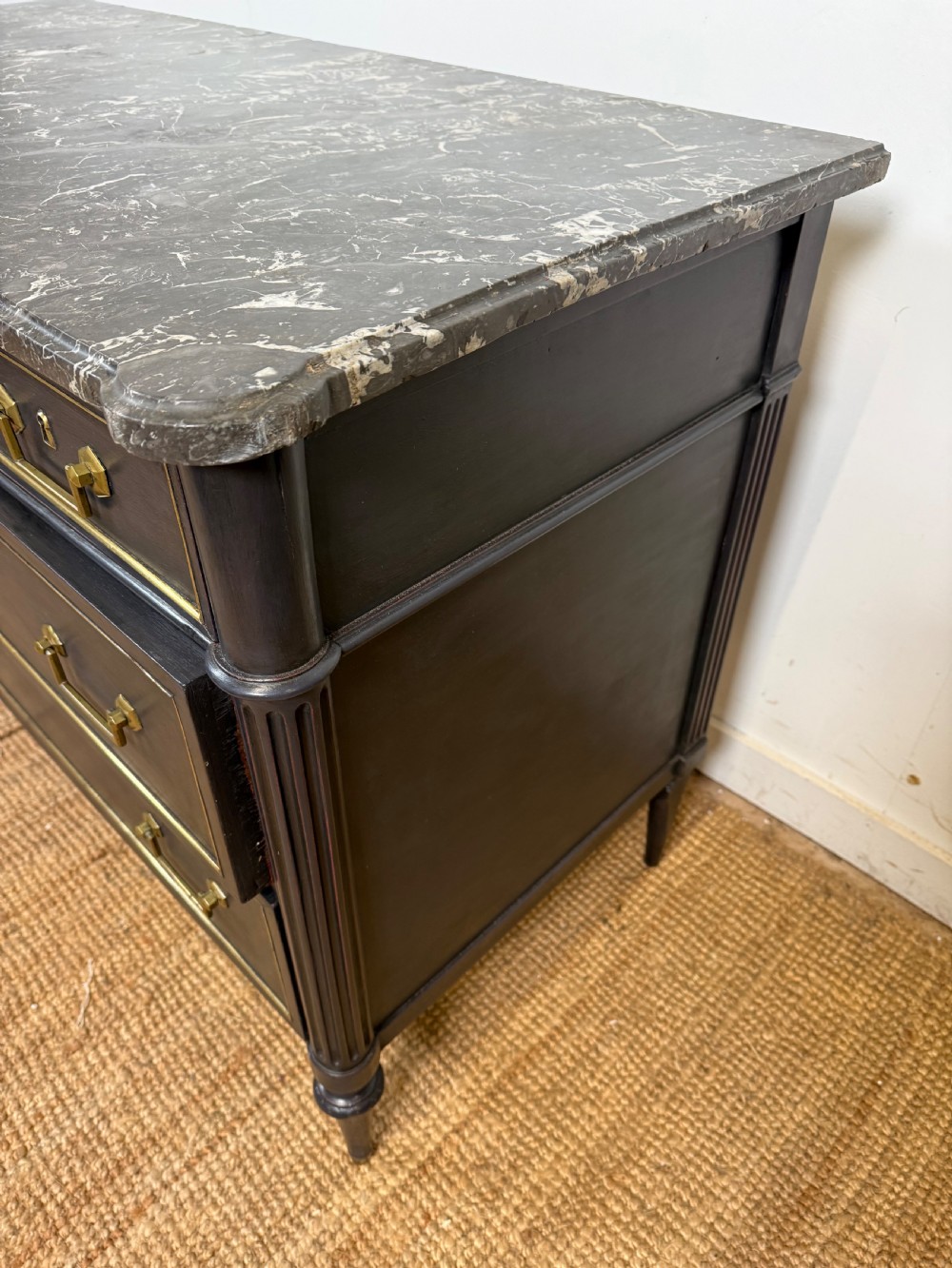 An early 19th-century black painted Louis XVI style commode featuring a grey marble top, brass trim, and fluted column legs. View XIV