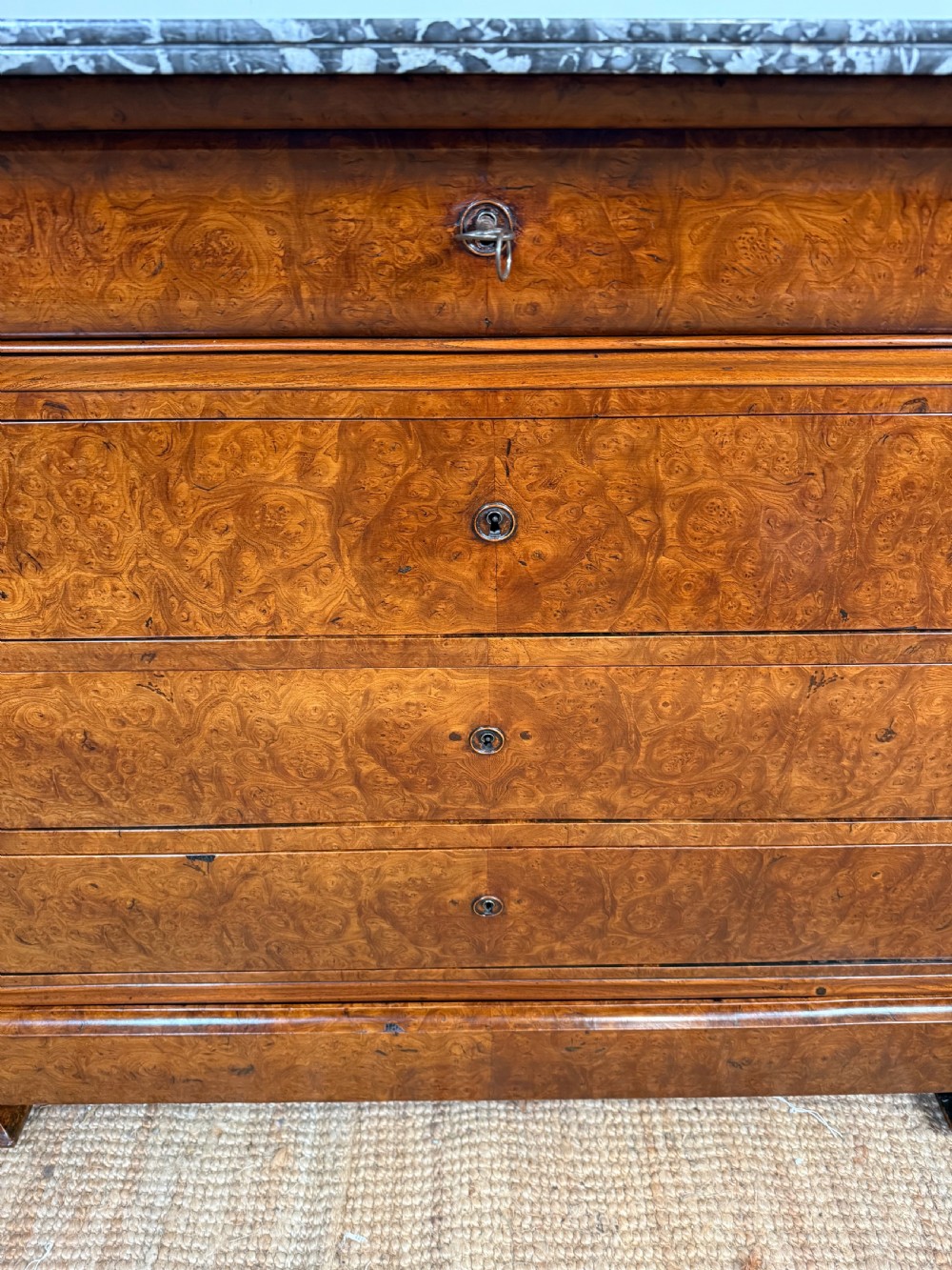 A rectangular 19th-century burr elm commode featuring a grey mottled marble top and three long drawers with central key escutcheons. View II