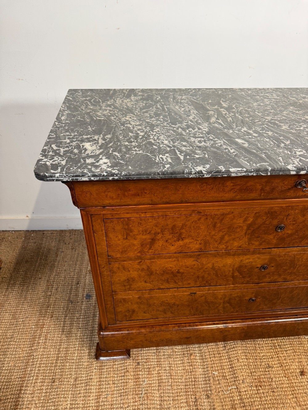 A rectangular 19th-century burr elm commode featuring a grey mottled marble top and three long drawers with central key escutcheons. View V
