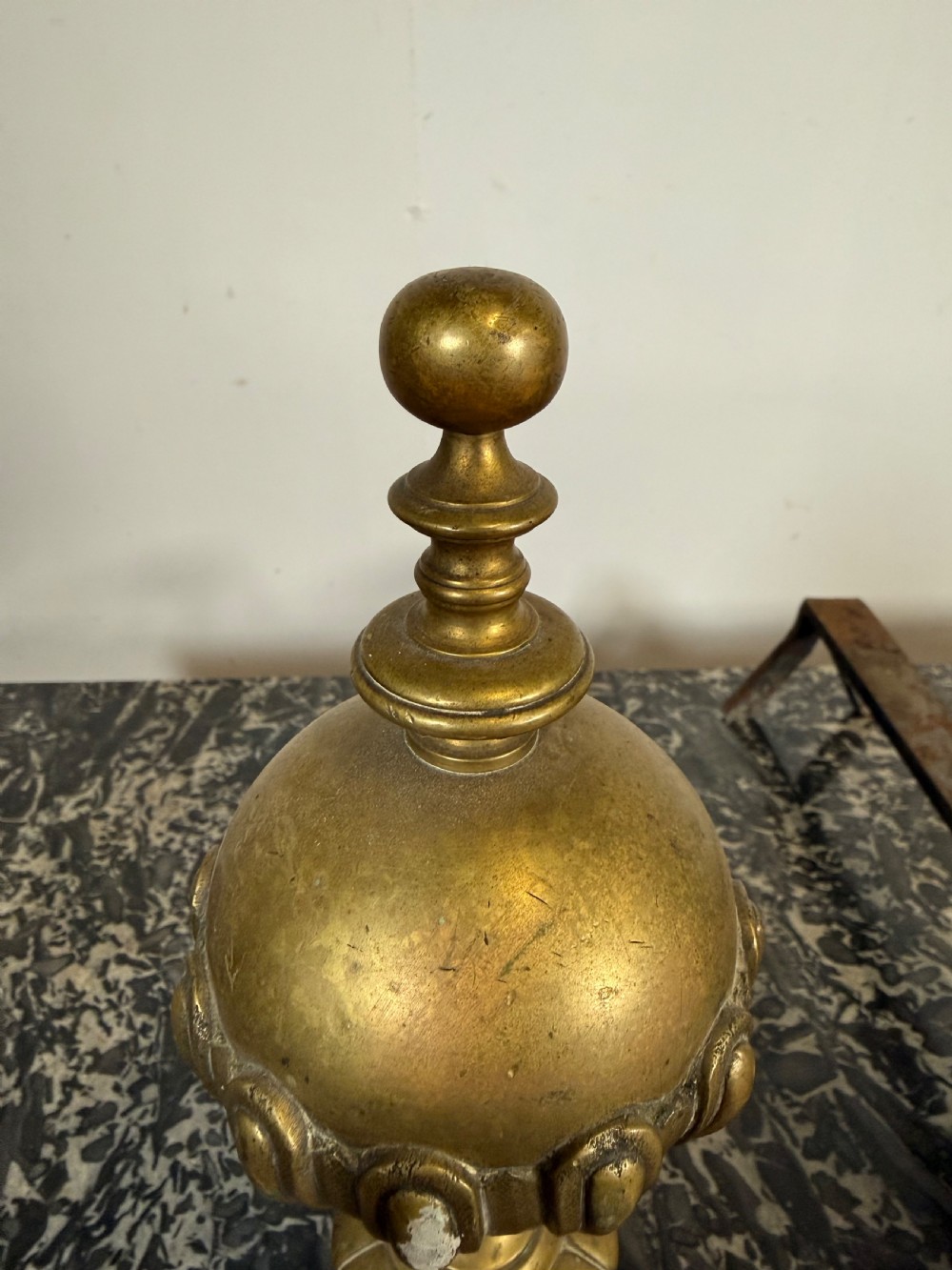 A pair of antique brass fire dogs featuring urn finials, gadrooned details, relief-carved creature bases, and iron billet bars. View VII