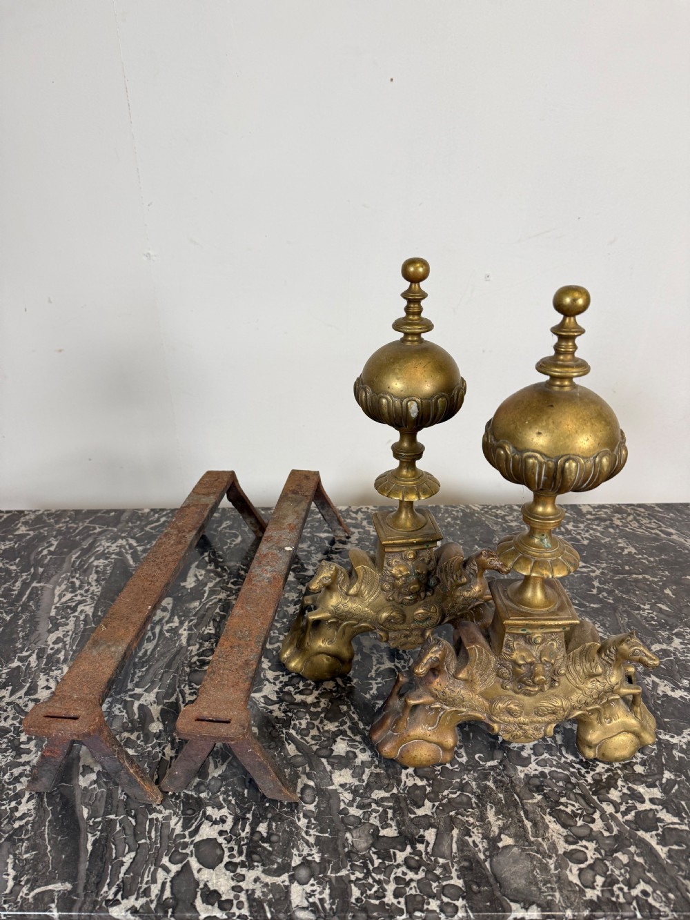 A pair of antique brass fire dogs featuring urn finials, gadrooned details, relief-carved creature bases, and iron billet bars. View VIII