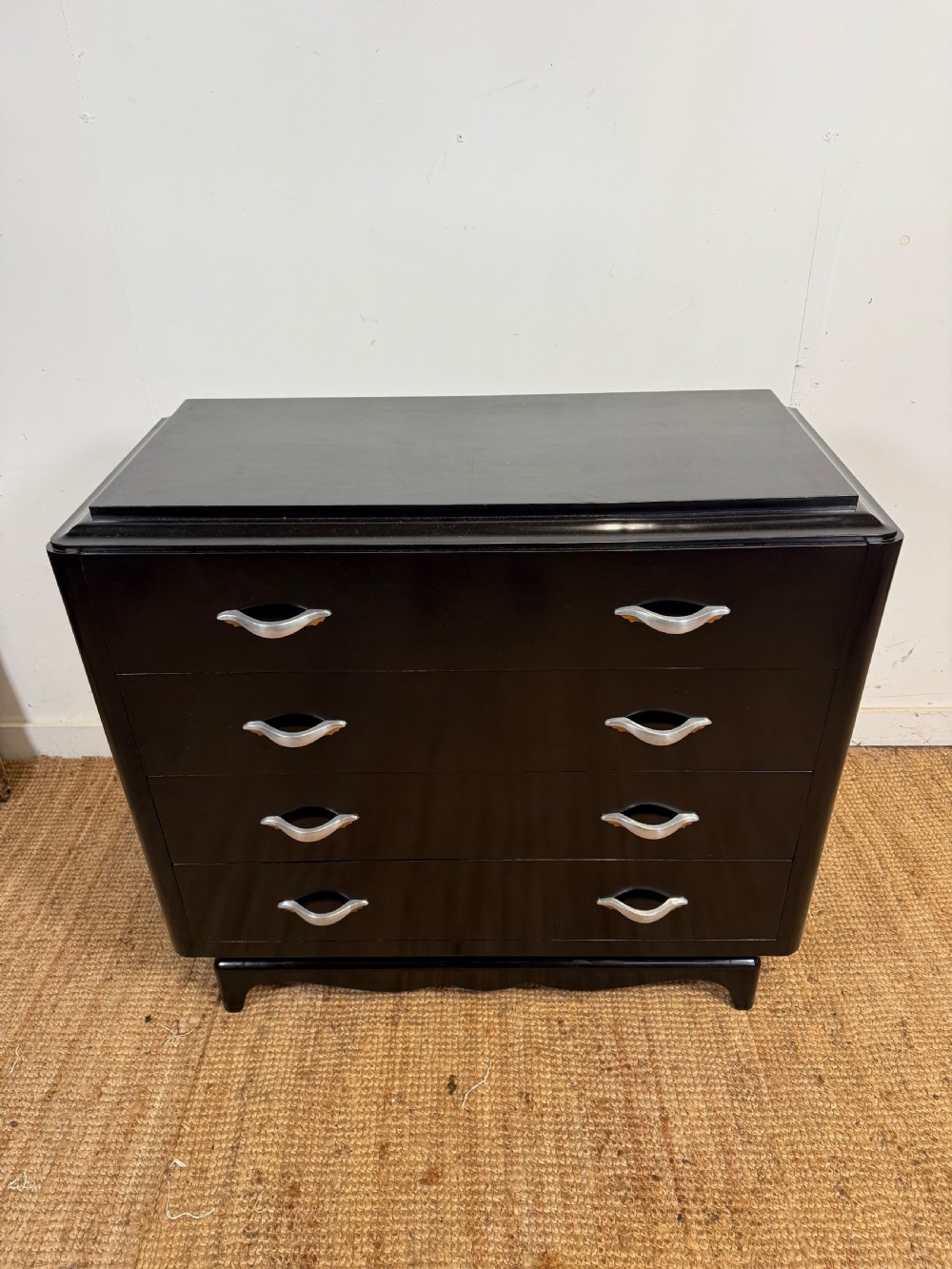 A French Art Deco ebonised black wooden commode featuring four stacked drawers with curved silver metal handles and a stepped top border.