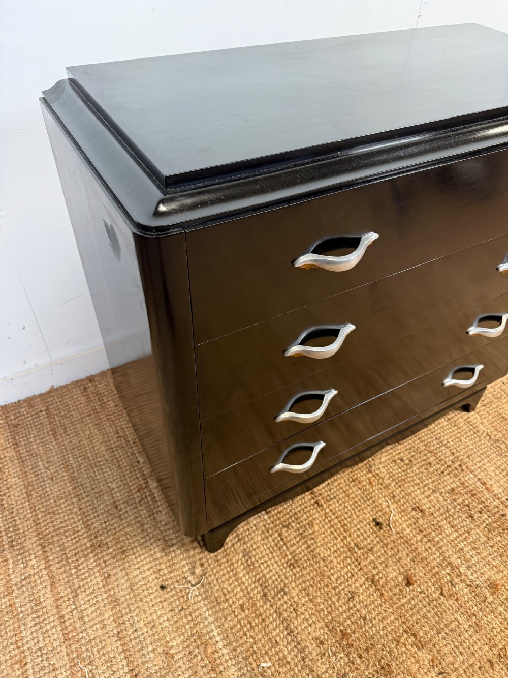 A French Art Deco ebonised black wooden commode featuring four stacked drawers with curved silver metal handles and a stepped top border. View II