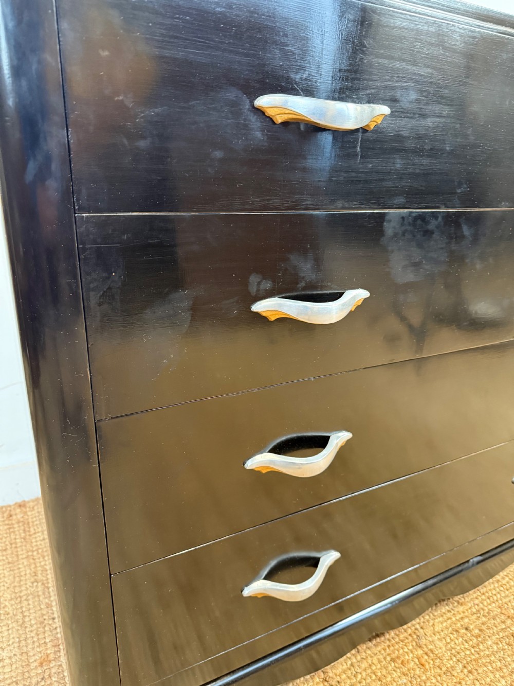 A French Art Deco ebonised black wooden commode featuring four stacked drawers with curved silver metal handles and a stepped top border. View III