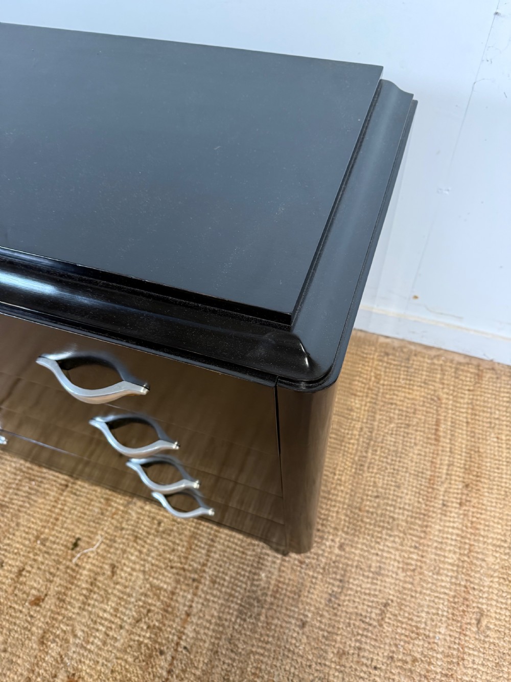 A French Art Deco ebonised black wooden commode featuring four stacked drawers with curved silver metal handles and a stepped top border. View V