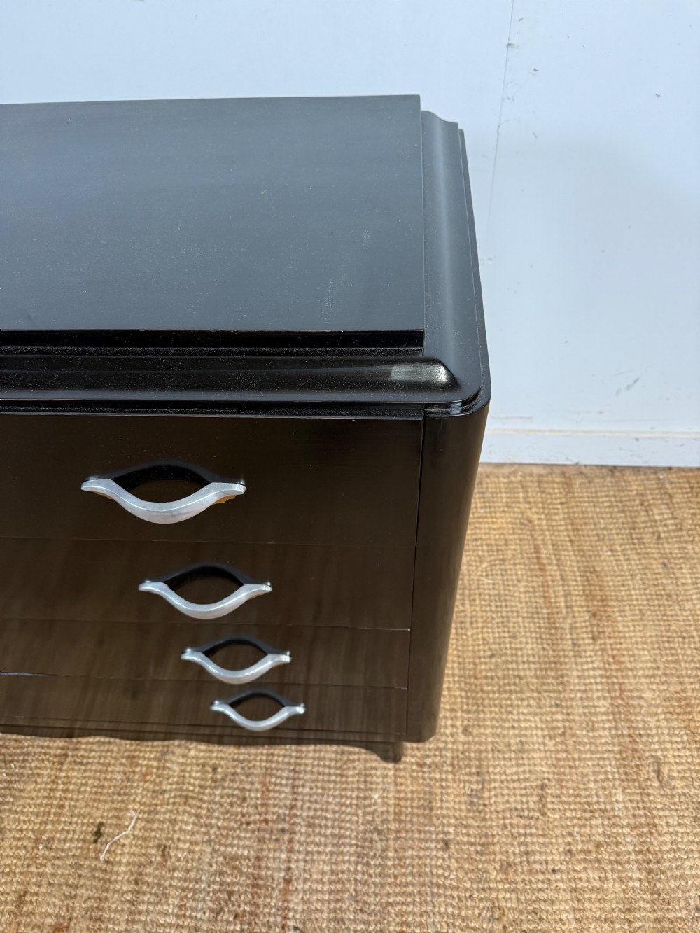 A French Art Deco ebonised black wooden commode featuring four stacked drawers with curved silver metal handles and a stepped top border. View VI