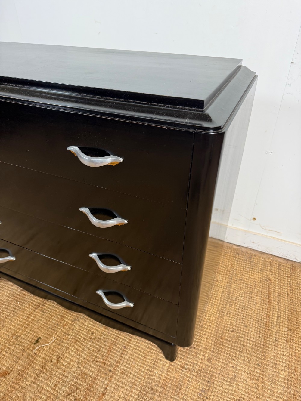 A French Art Deco ebonised black wooden commode featuring four stacked drawers with curved silver metal handles and a stepped top border. View VII