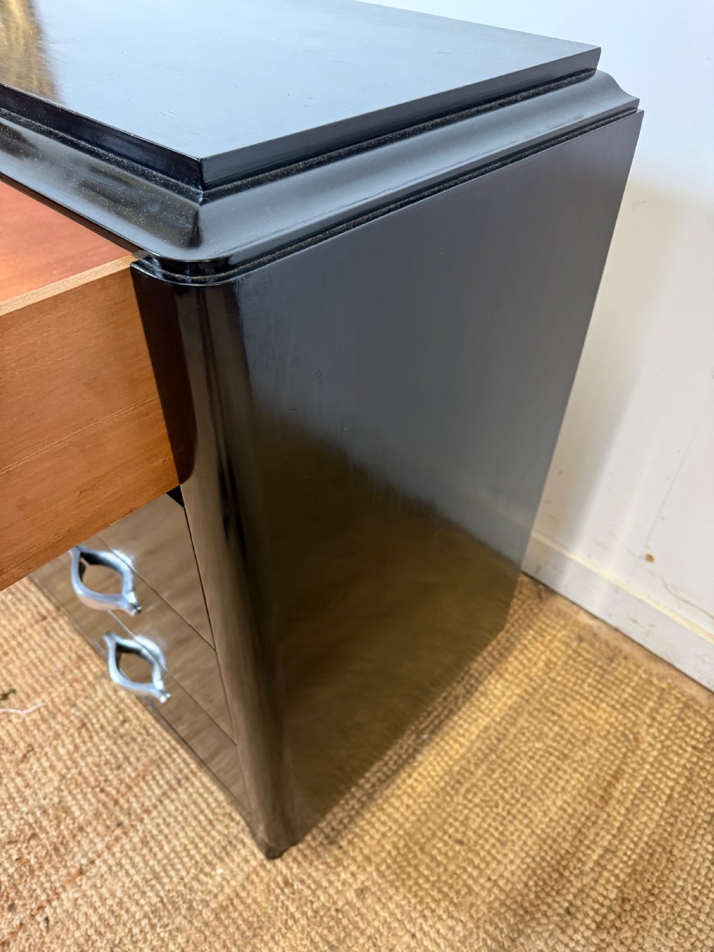 A French Art Deco ebonised black wooden commode featuring four stacked drawers with curved silver metal handles and a stepped top border. View IX