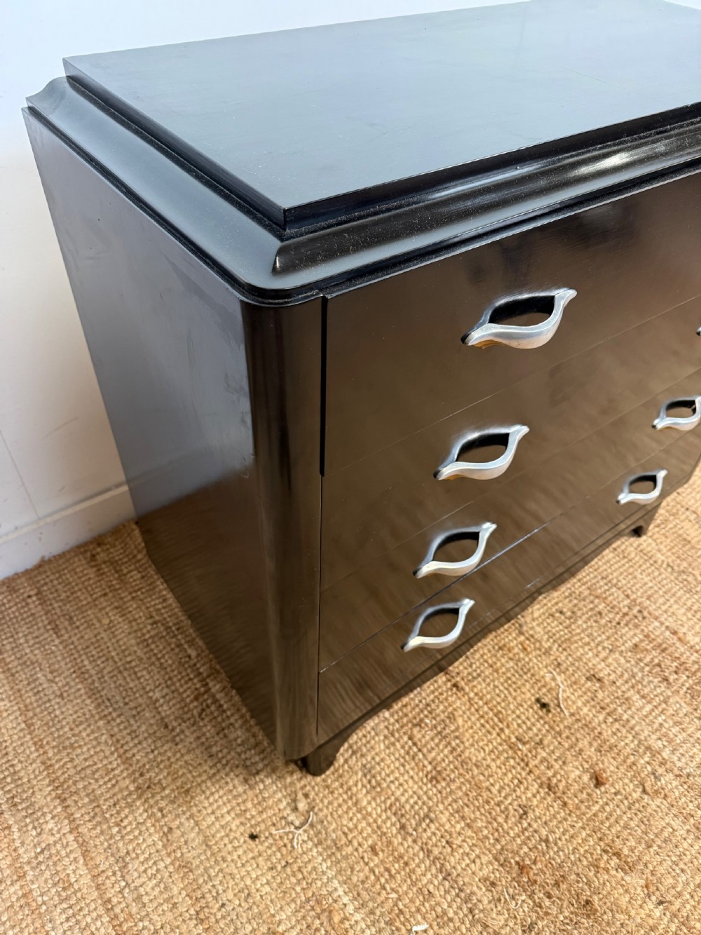 A French Art Deco ebonised black wooden commode featuring four stacked drawers with curved silver metal handles and a stepped top border. View X