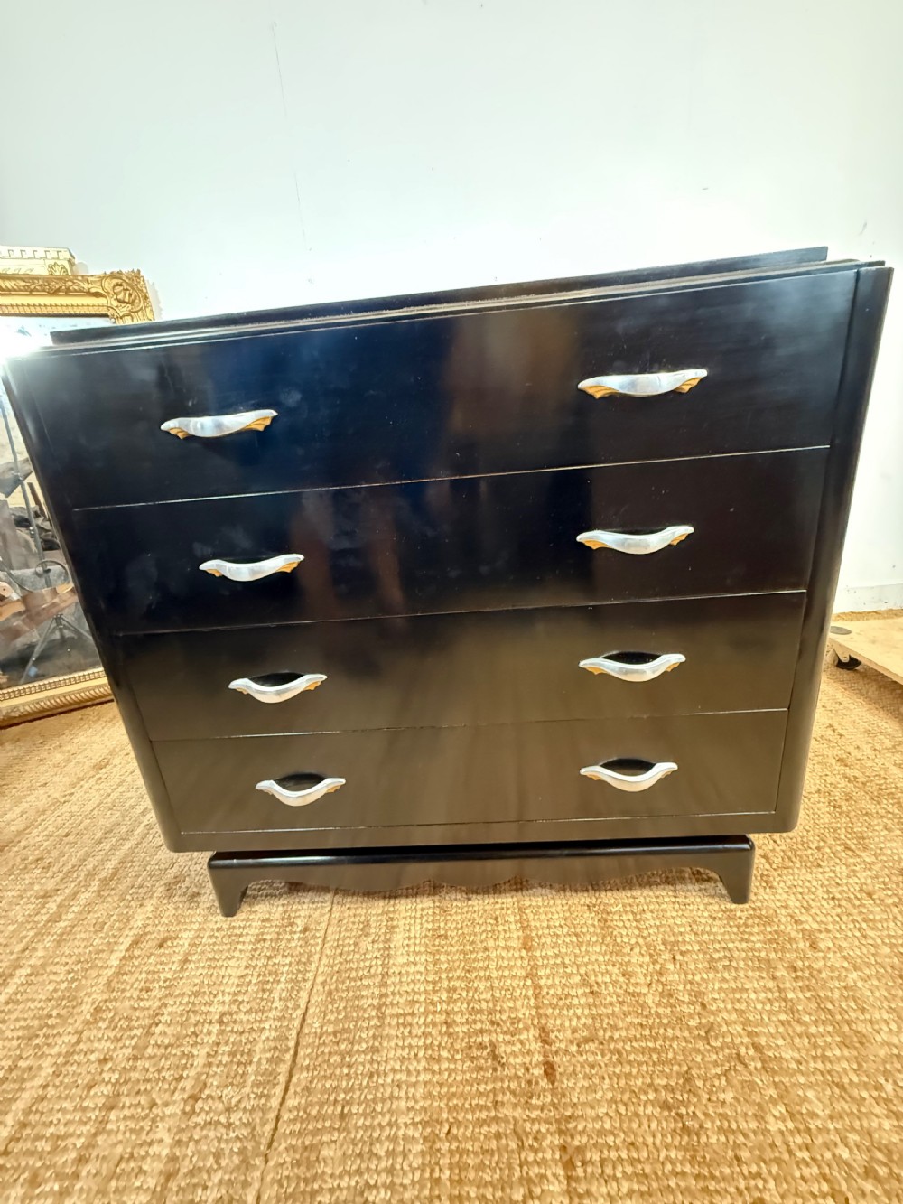 A French Art Deco ebonised black wooden commode featuring four stacked drawers with curved silver metal handles and a stepped top border. View XIV