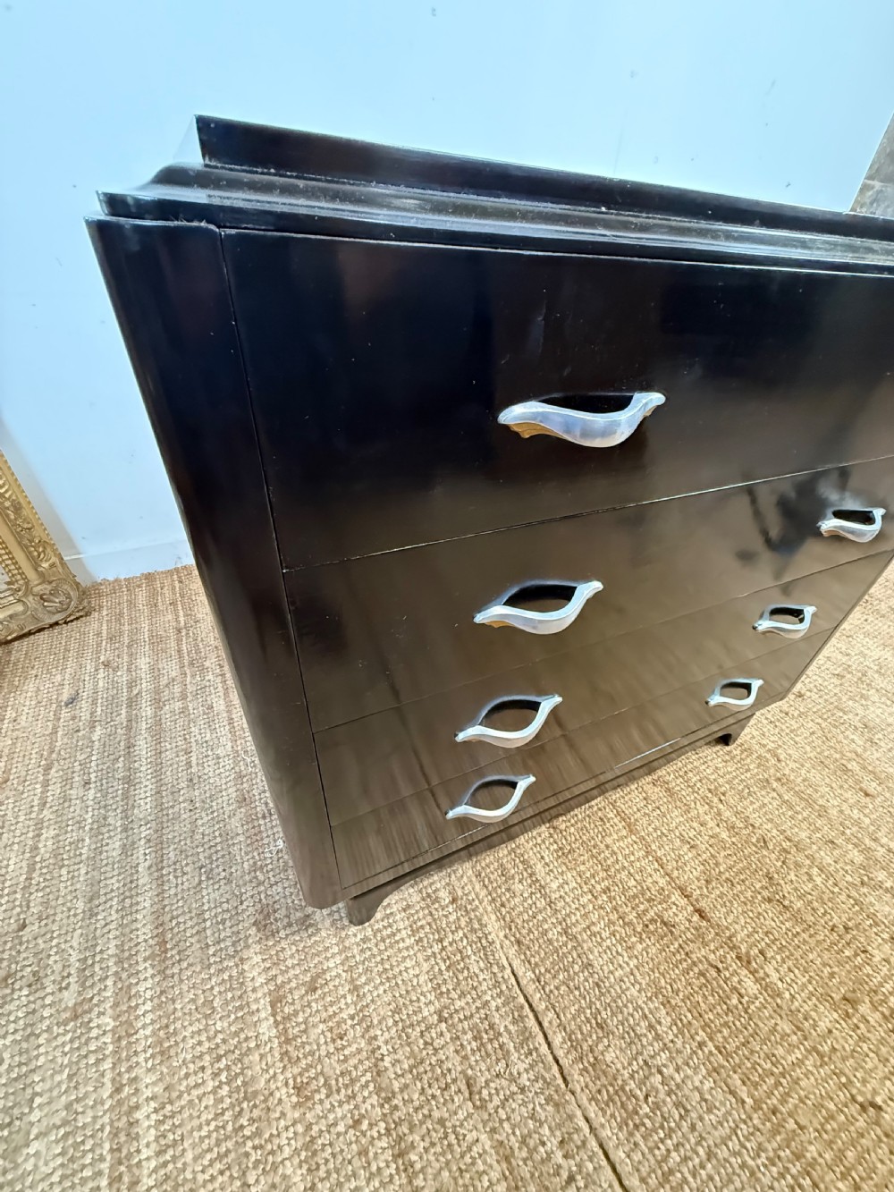 A French Art Deco ebonised black wooden commode featuring four stacked drawers with curved silver metal handles and a stepped top border. View XV