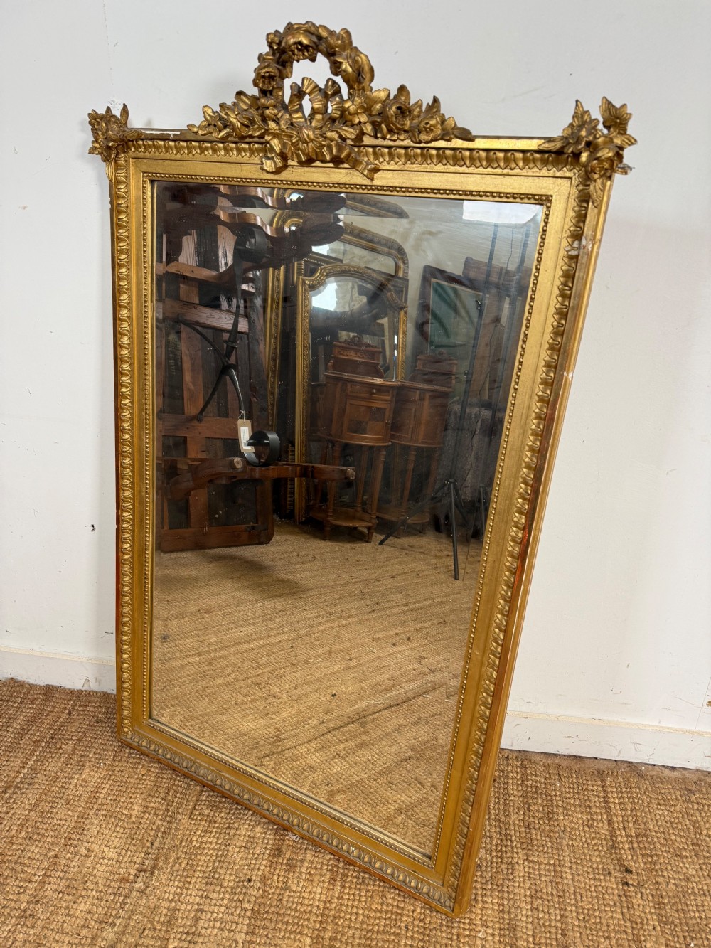 A rectangular antique wall mirror featuring a prominent ornate floral and ribbon carved crest in a gilded finish.