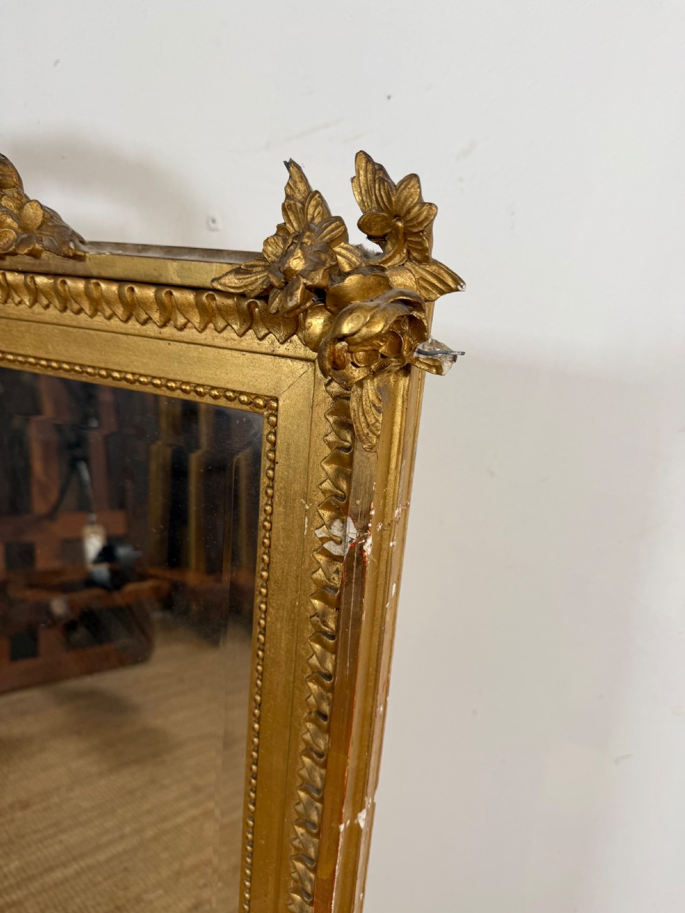 A rectangular antique wall mirror featuring a prominent ornate floral and ribbon carved crest in a gilded finish. View II