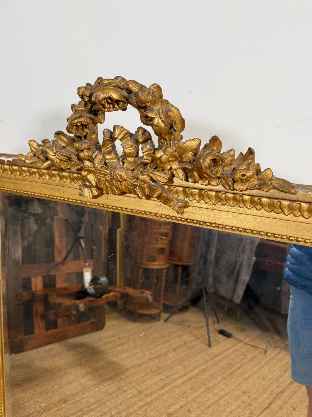 A rectangular antique wall mirror featuring a prominent ornate floral and ribbon carved crest in a gilded finish. View III