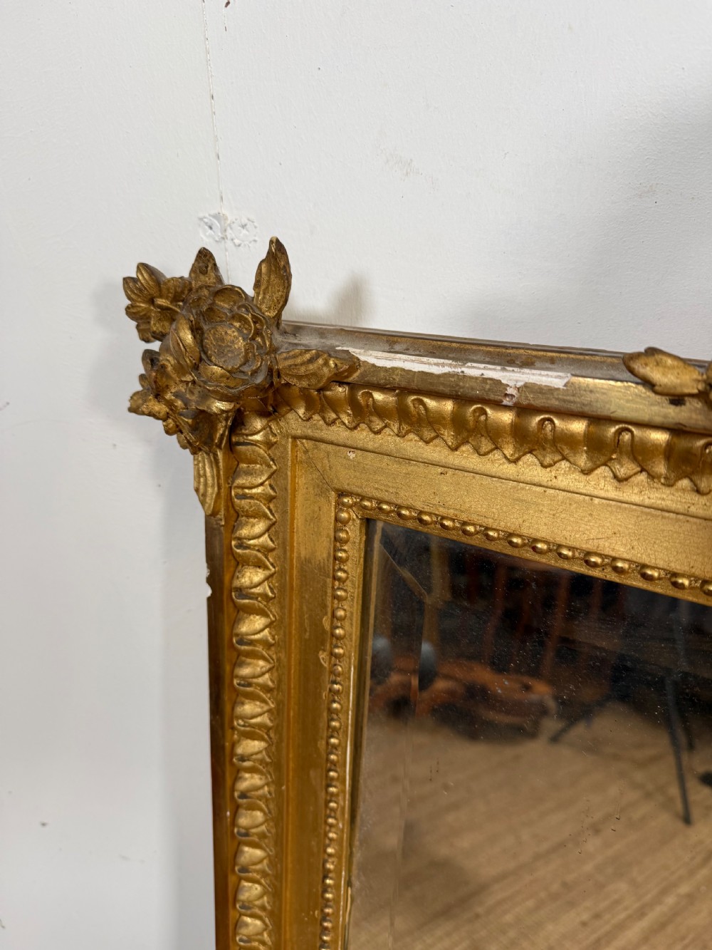 A rectangular antique wall mirror featuring a prominent ornate floral and ribbon carved crest in a gilded finish. View V