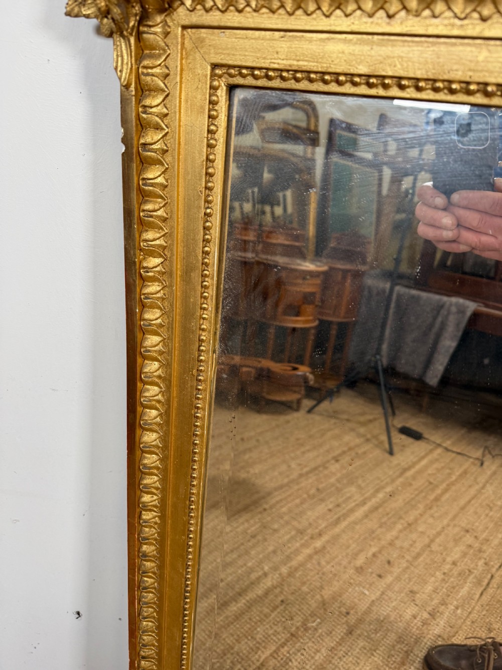 A rectangular antique wall mirror featuring a prominent ornate floral and ribbon carved crest in a gilded finish. View VI