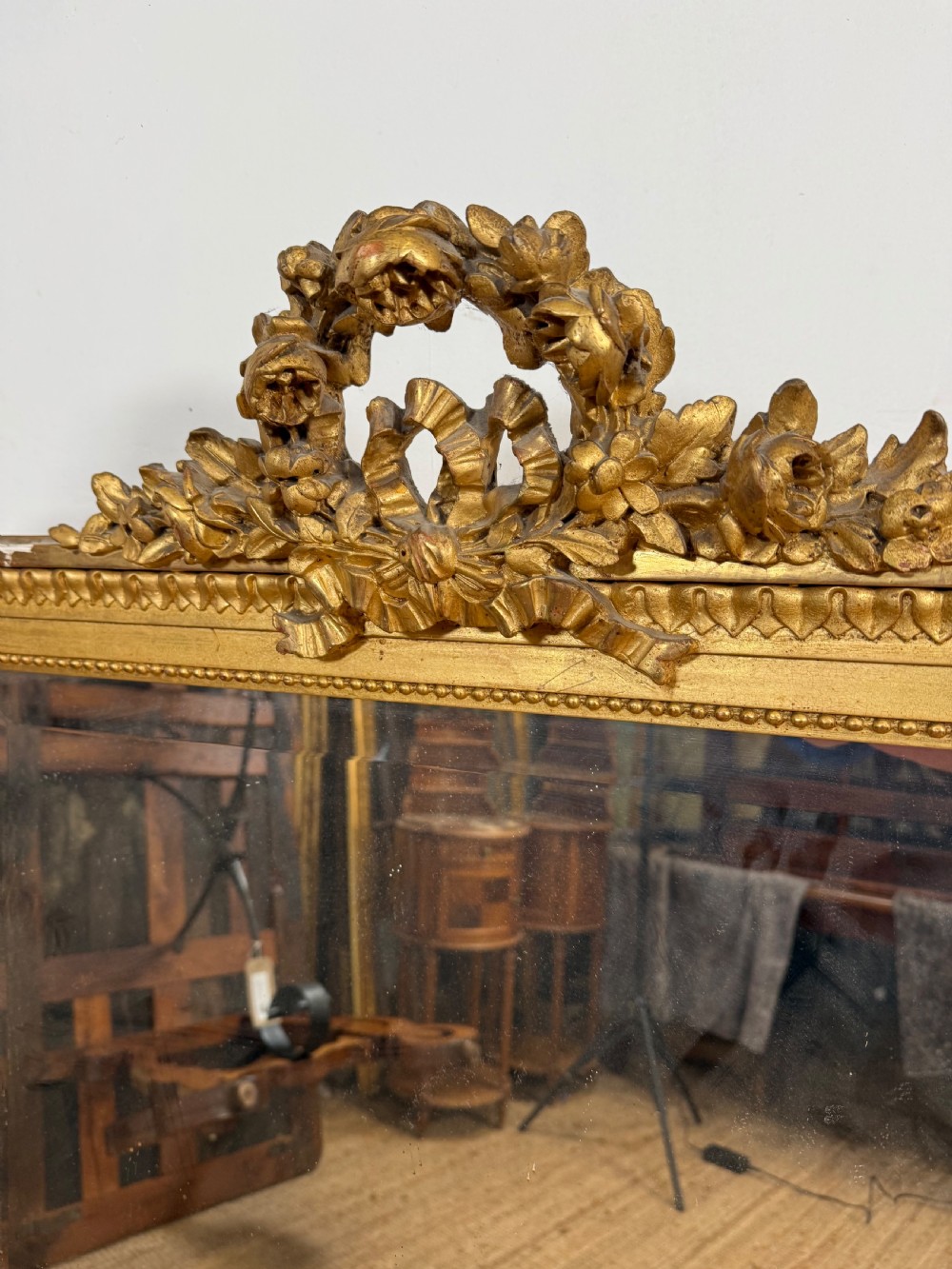 A rectangular antique wall mirror featuring a prominent ornate floral and ribbon carved crest in a gilded finish. View XII