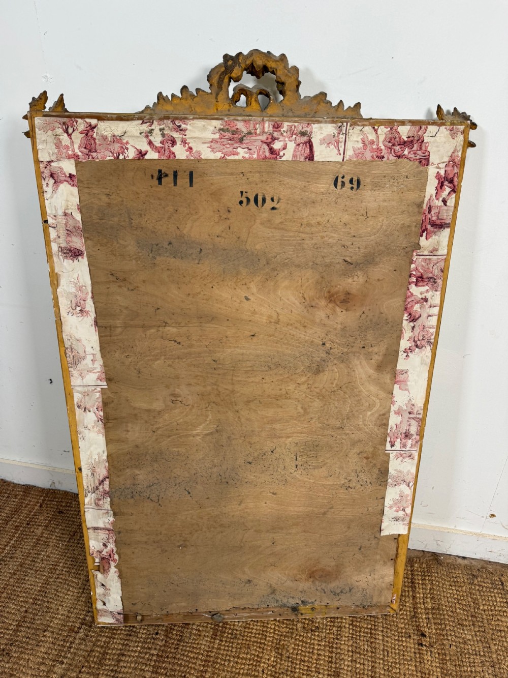 A rectangular antique wall mirror featuring a prominent ornate floral and ribbon carved crest in a gilded finish. View XIII