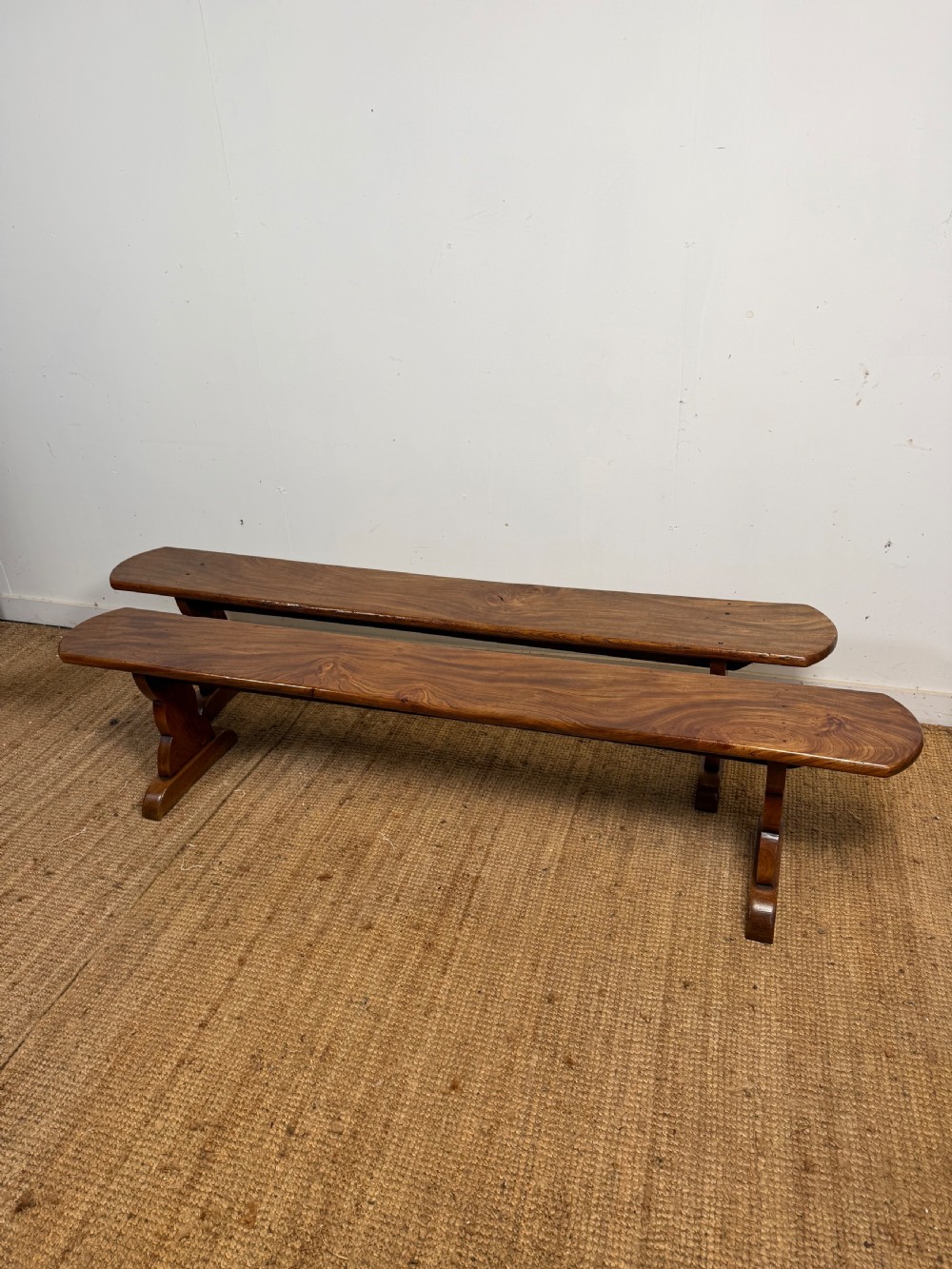 A pair of early 20th-century French rustic benches crafted from solid warm brown elm with visible wood grain and trestle end supports.
