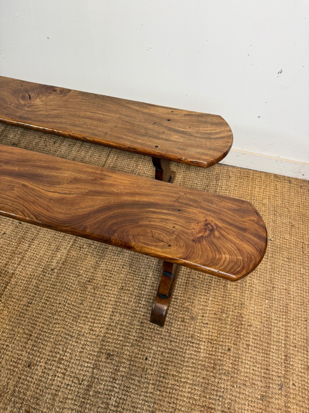 A pair of early 20th-century French rustic benches crafted from solid warm brown elm with visible wood grain and trestle end supports. View II