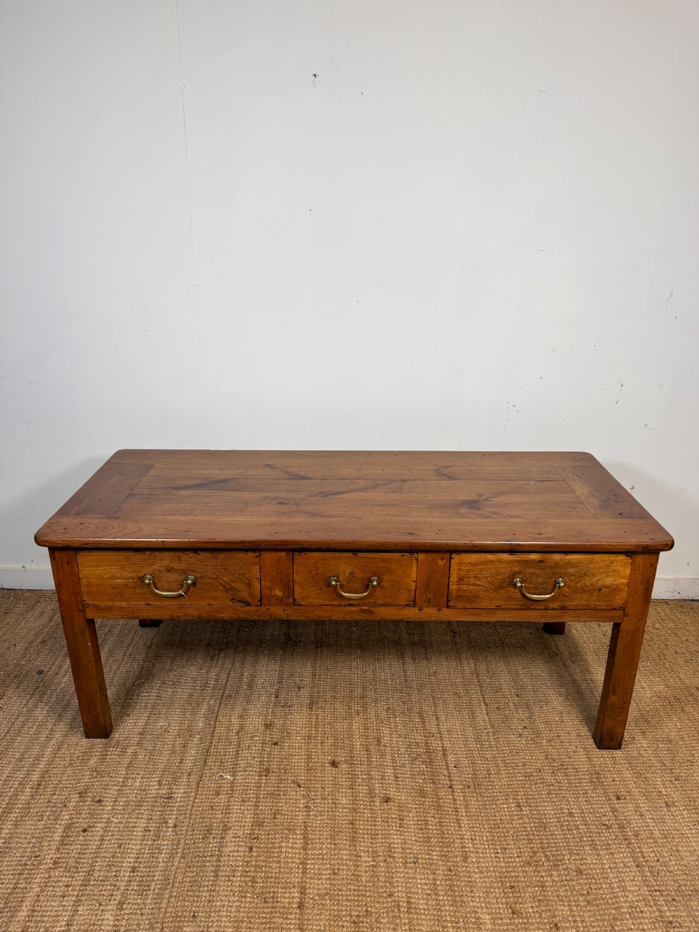 A 19th-century French provincial wooden dresser base featuring three drawers with brass bail handles set on straight legs.