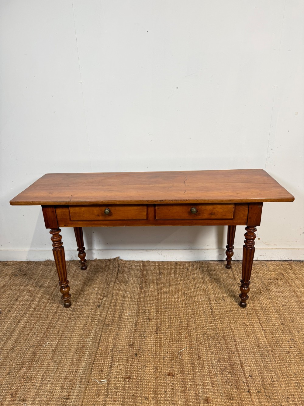A 19th-century French cherrywood console table featuring two frieze drawers with brass knobs and four turned, fluted legs.