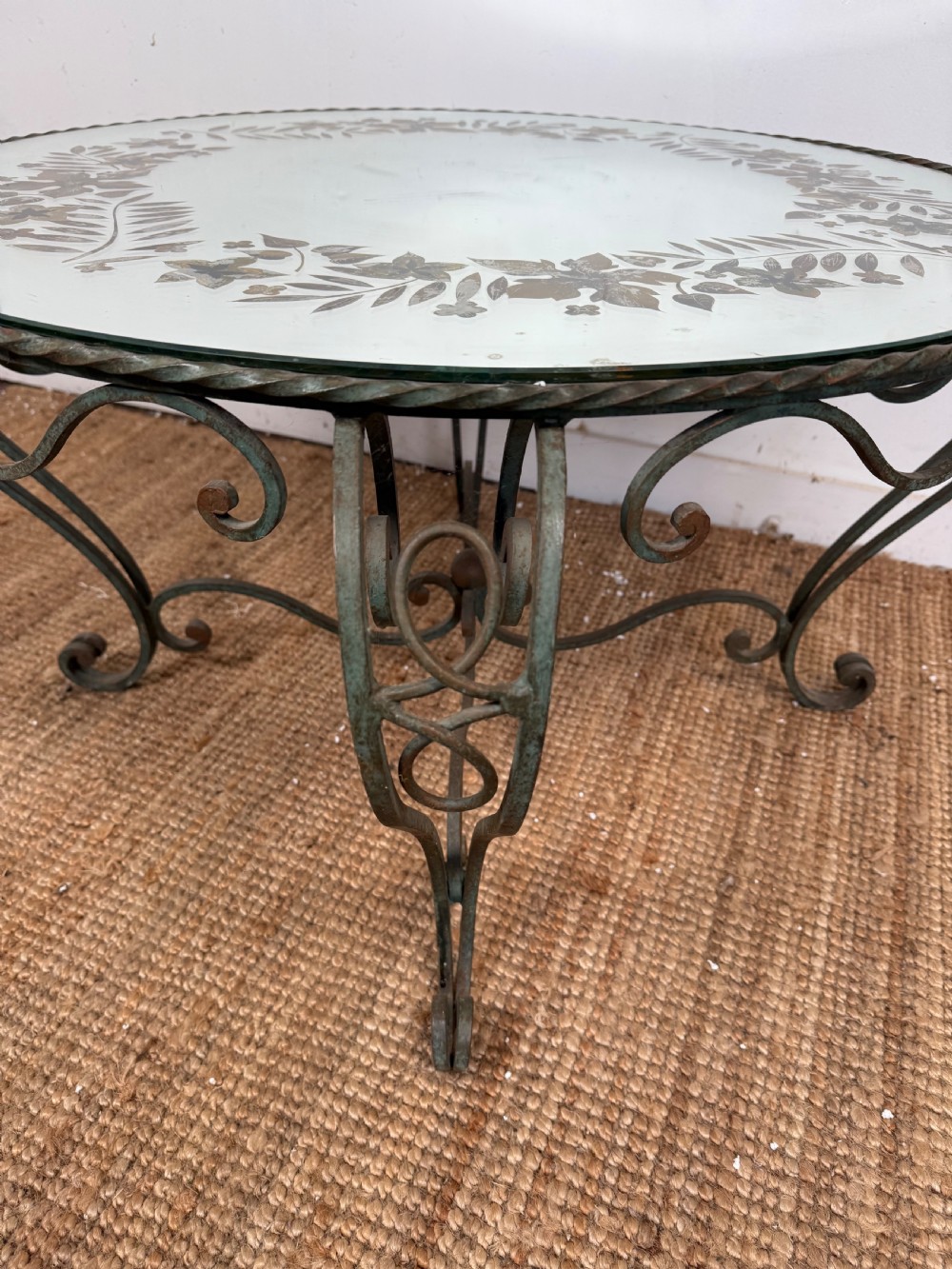 A round Art Deco coffee table featuring a verdigris wrought iron frame with scroll legs and a circular glass top decorated with a painted floral border. View II