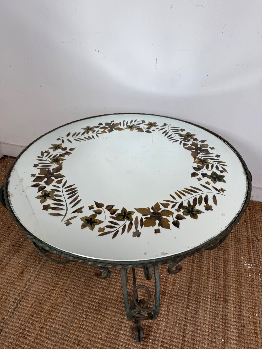 A round Art Deco coffee table featuring a verdigris wrought iron frame with scroll legs and a circular glass top decorated with a painted floral border. View III