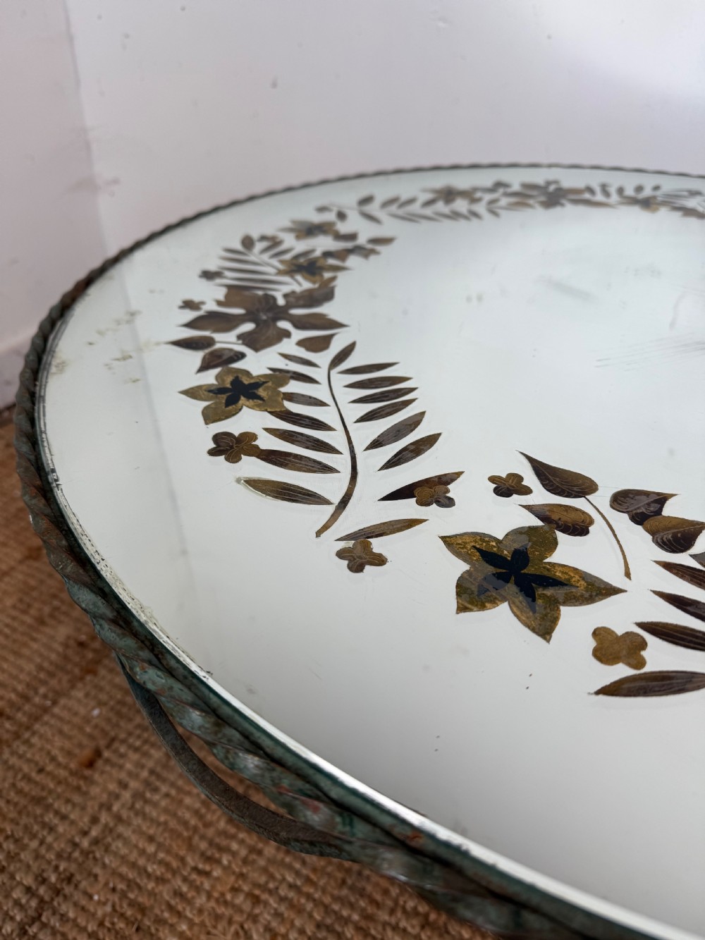 A round Art Deco coffee table featuring a verdigris wrought iron frame with scroll legs and a circular glass top decorated with a painted floral border. View VI