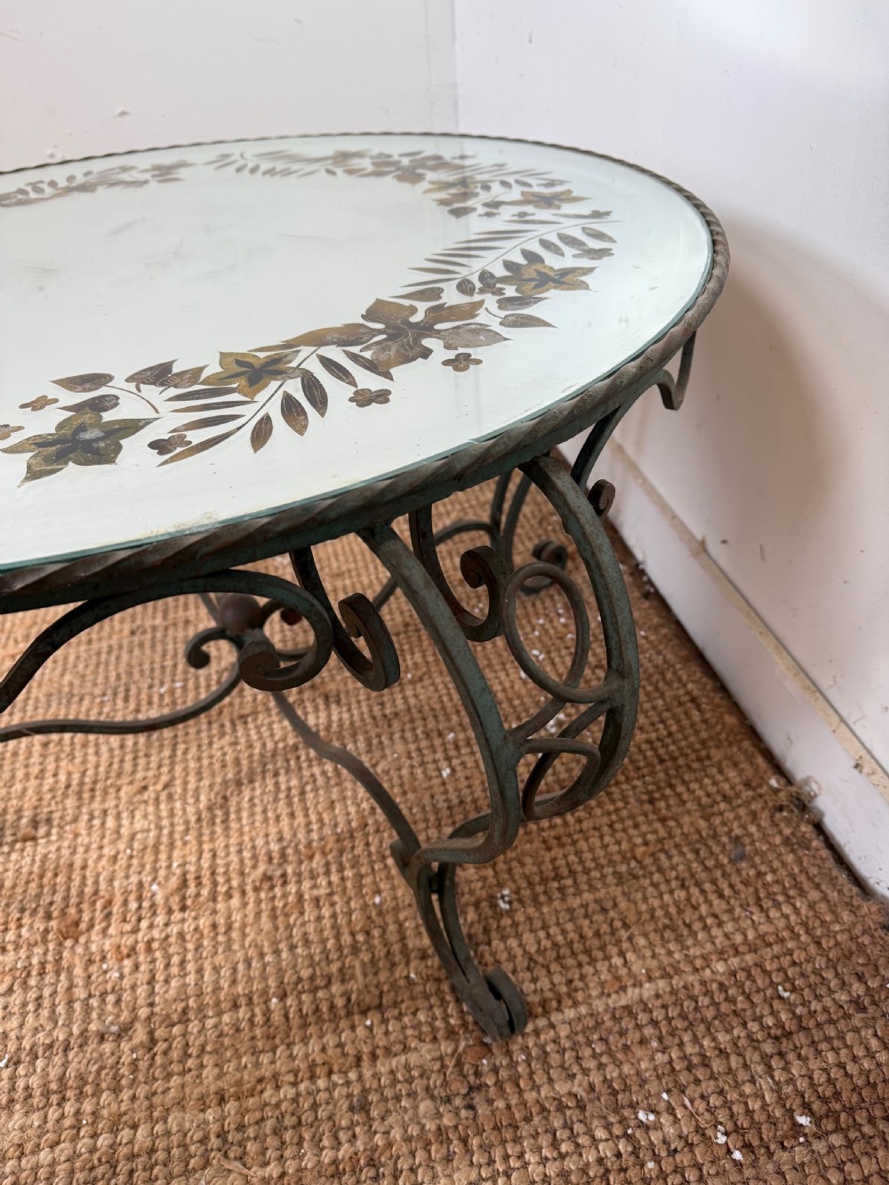 A round Art Deco coffee table featuring a verdigris wrought iron frame with scroll legs and a circular glass top decorated with a painted floral border. View VII
