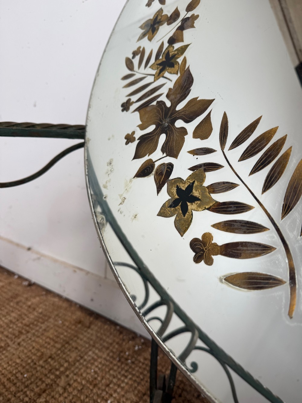 A round Art Deco coffee table featuring a verdigris wrought iron frame with scroll legs and a circular glass top decorated with a painted floral border. View XIII