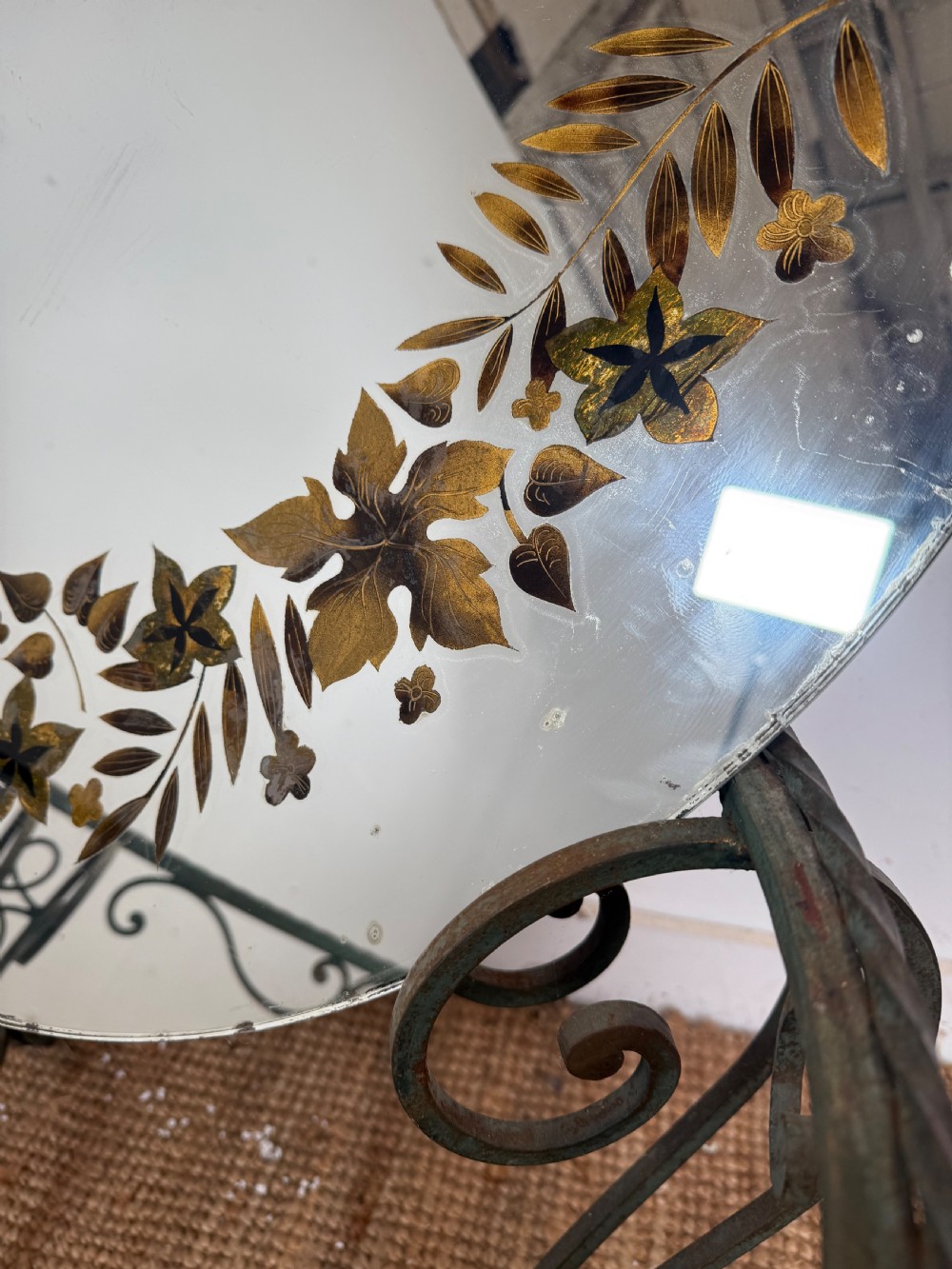 A round Art Deco coffee table featuring a verdigris wrought iron frame with scroll legs and a circular glass top decorated with a painted floral border. View XIV