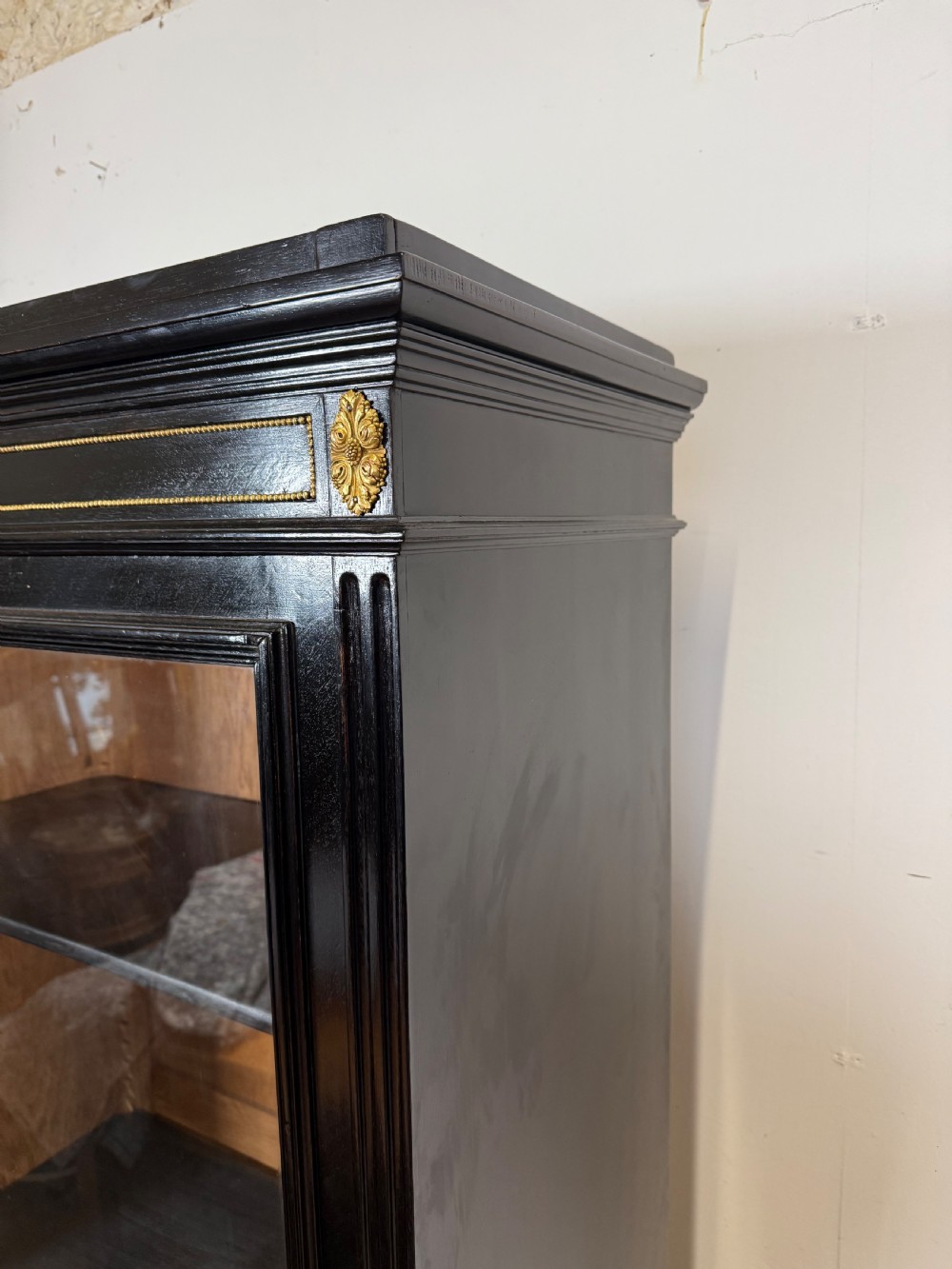 A narrow 19th-century Napoleon III ebonised wooden bookcase featuring a single glazed glass door, decorative gilt brass mounts, and a warm oak lined interior. View II
