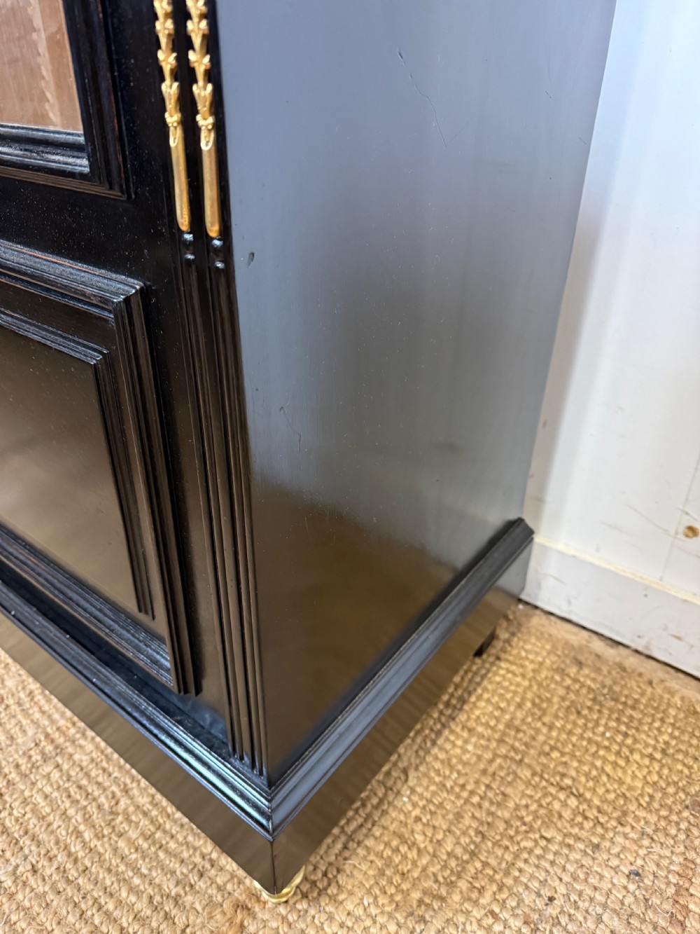A narrow 19th-century Napoleon III ebonised wooden bookcase featuring a single glazed glass door, decorative gilt brass mounts, and a warm oak lined interior. View IV