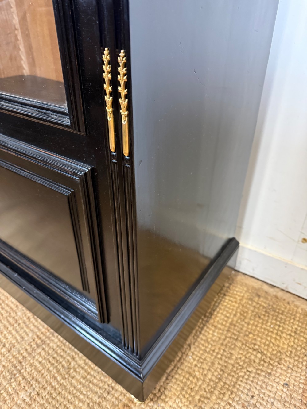 A narrow 19th-century Napoleon III ebonised wooden bookcase featuring a single glazed glass door, decorative gilt brass mounts, and a warm oak lined interior. View V