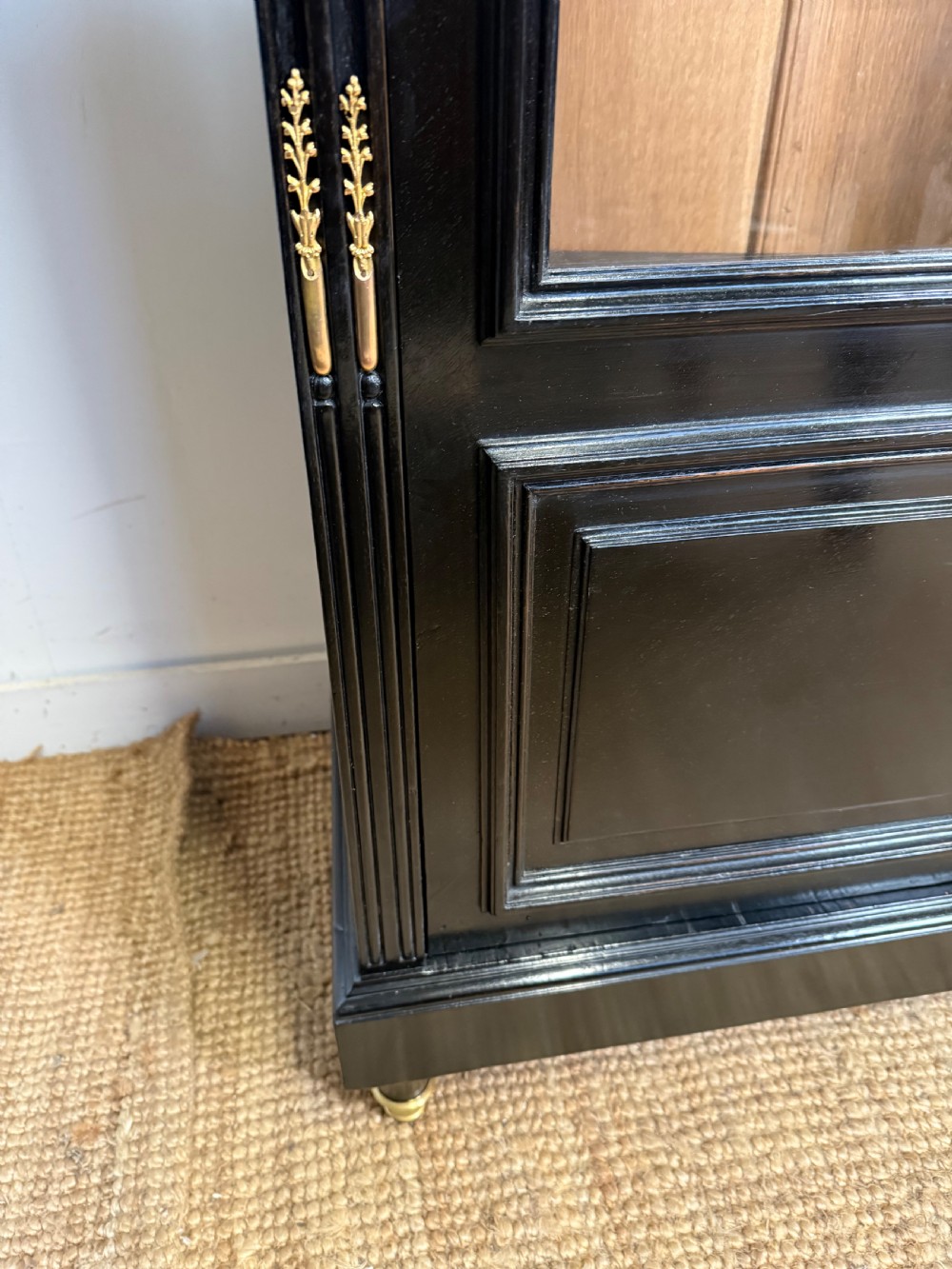 A narrow 19th-century Napoleon III ebonised wooden bookcase featuring a single glazed glass door, decorative gilt brass mounts, and a warm oak lined interior. View VIII