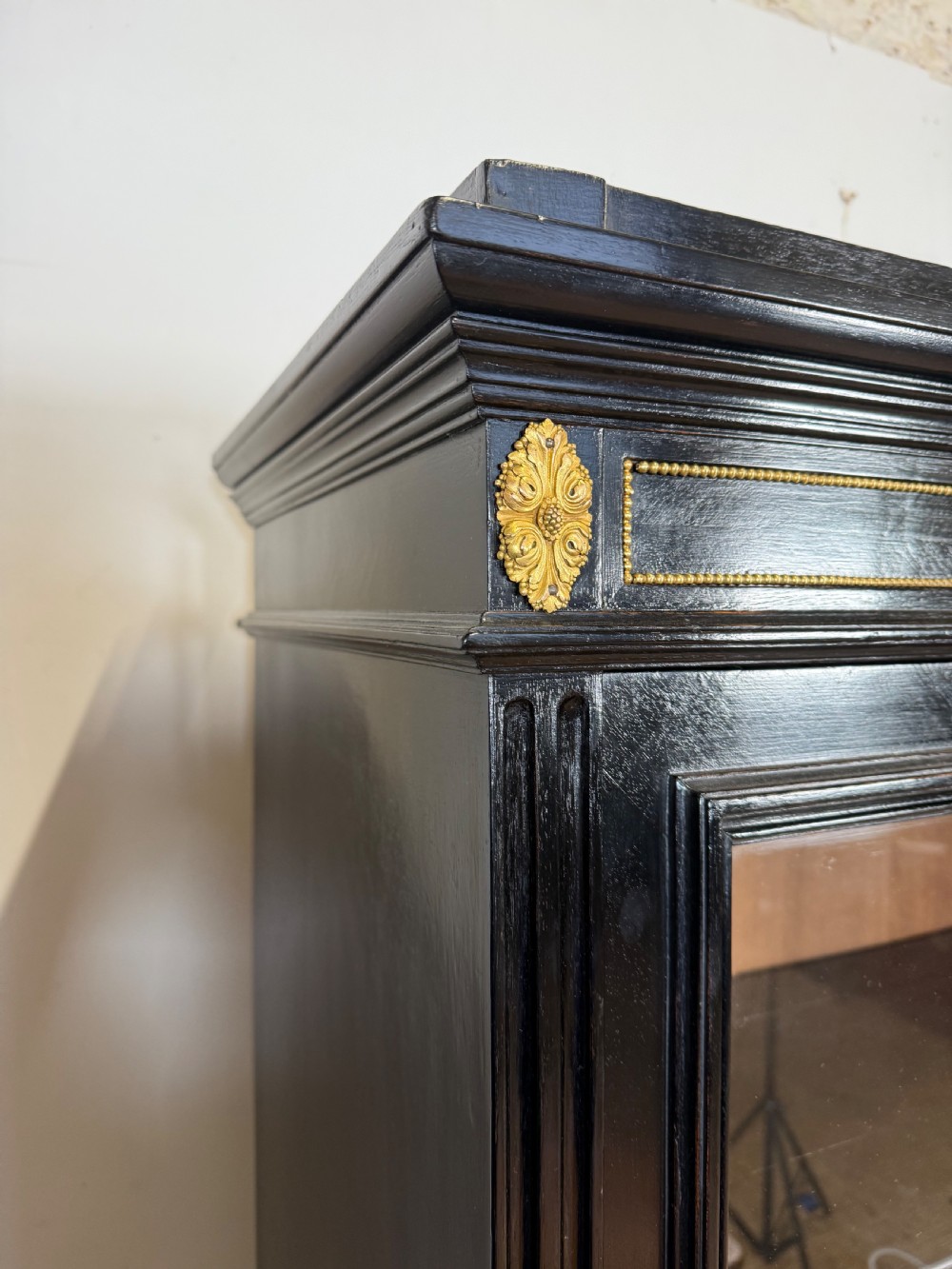 A narrow 19th-century Napoleon III ebonised wooden bookcase featuring a single glazed glass door, decorative gilt brass mounts, and a warm oak lined interior. View IX