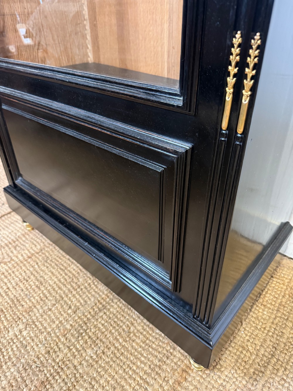 A narrow 19th-century Napoleon III ebonised wooden bookcase featuring a single glazed glass door, decorative gilt brass mounts, and a warm oak lined interior. View X