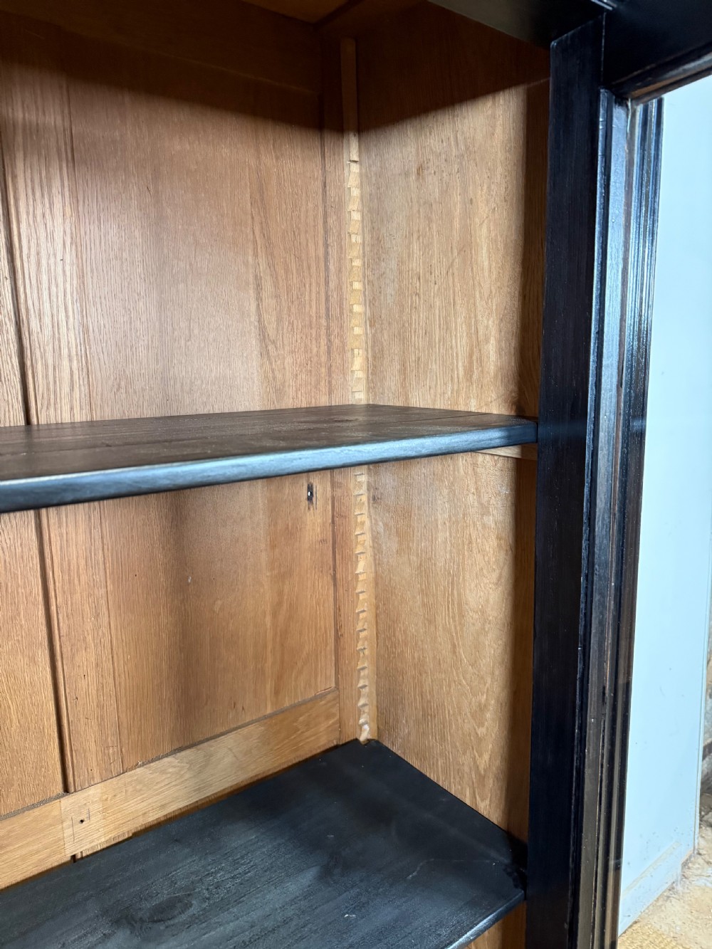 A narrow 19th-century Napoleon III ebonised wooden bookcase featuring a single glazed glass door, decorative gilt brass mounts, and a warm oak lined interior. View XI