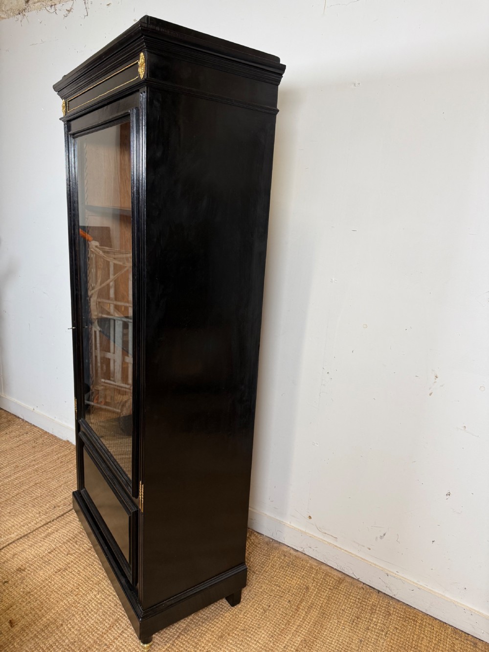 A narrow 19th-century Napoleon III ebonised wooden bookcase featuring a single glazed glass door, decorative gilt brass mounts, and a warm oak lined interior. View XIII