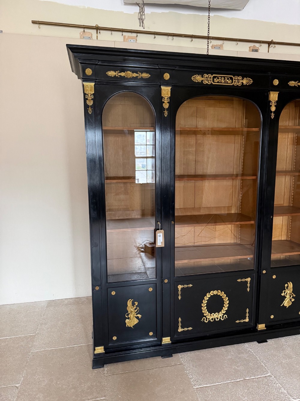 A large ebonised three-door glazed bookcase featuring gold-toned gilt-bronze mounts, arched glass panels, and an oak interior. View II